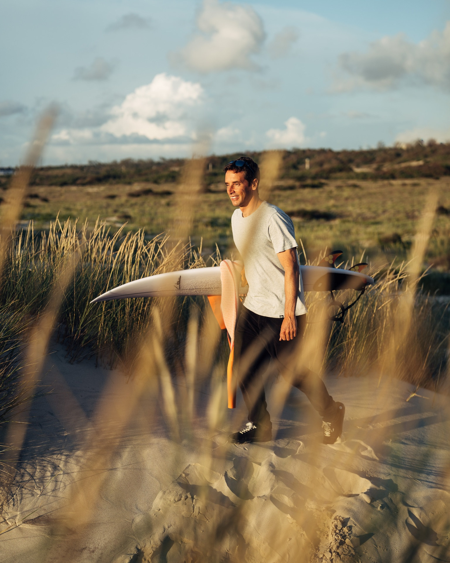 Ivo Cação walking through the dunes with his surfboard